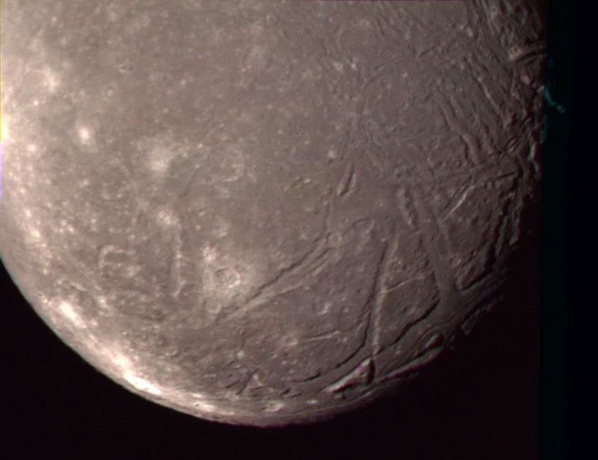 Voyager 2 color composite of Ariel showing cratered plains crossed by fault scarps and long valleys.