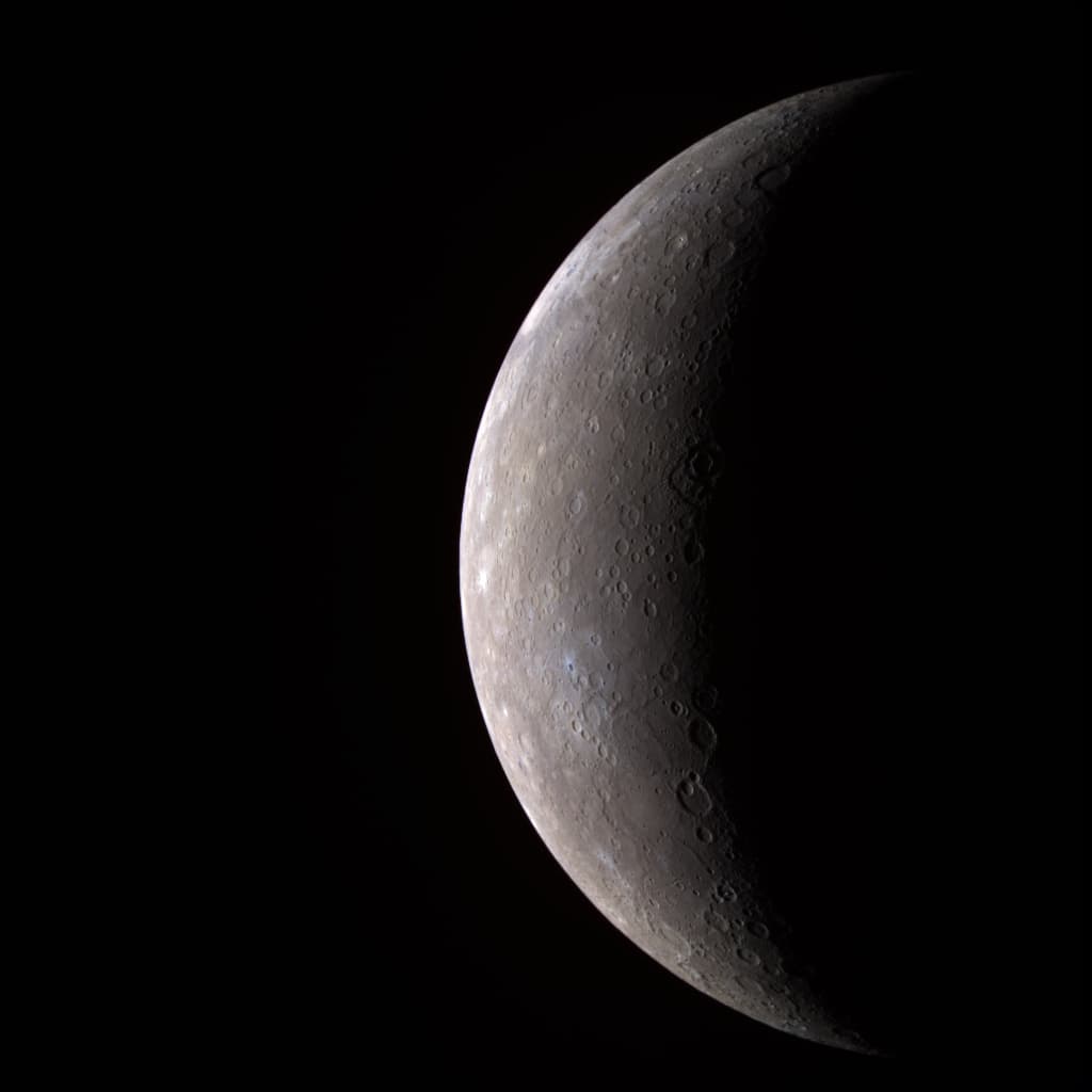 A false-colour MESSENGER view of Mercury as a round, cratered world, brightly lit on the left and fading into shadow on the right.