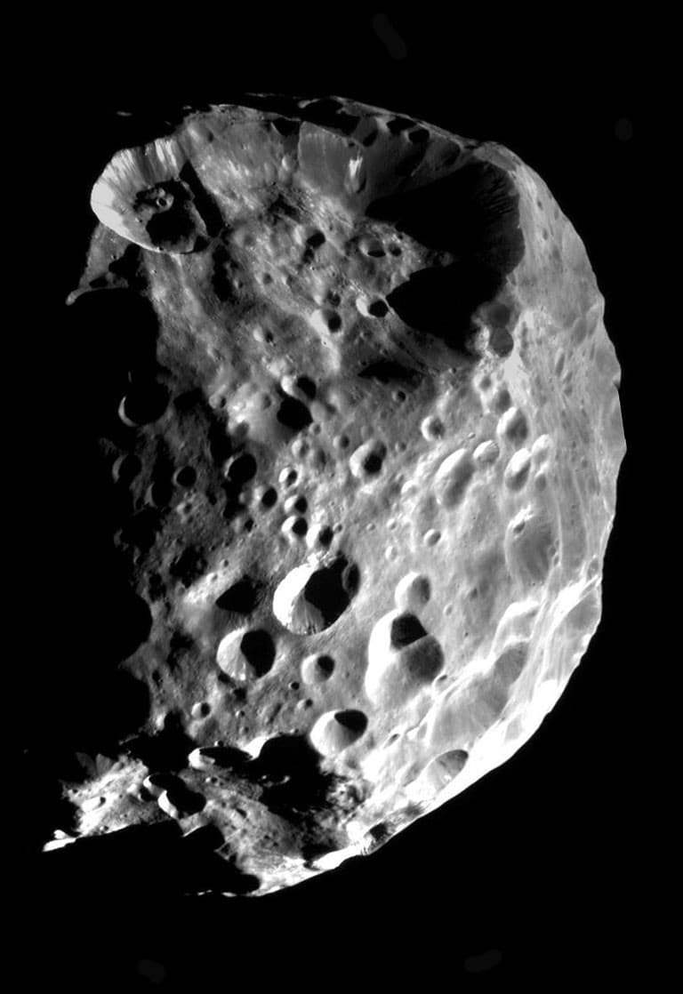 Cassini grayscale mosaic of dark, irregular Phoebe, showing overlapping craters and bright material exposed on crater walls.