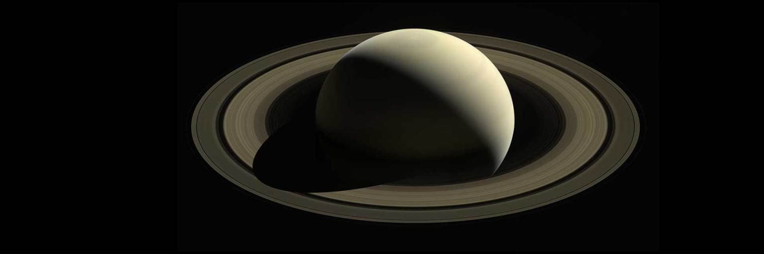 Saturn and its rings seen as a thin sunlit crescent against black space in a Cassini mosaic.