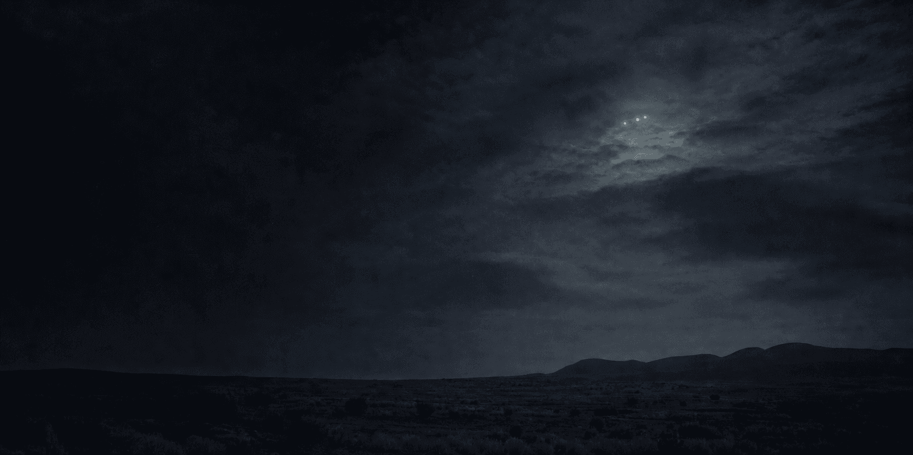 Three distant lights above a dark desert horizon beneath heavy clouds